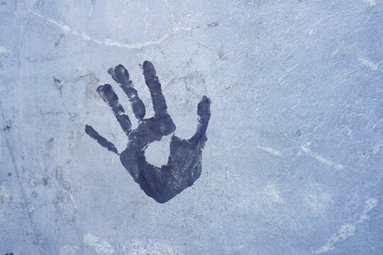 Close-up of a blue handprint on a painted concrete wall with rough texture and artistic appeal.