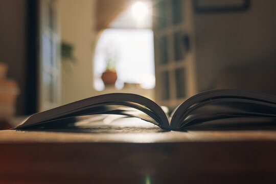 Open book resting on a wooden table with sunlight streaming through balcony door