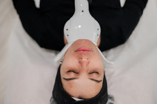 Female client lying on treatment bed receiving laser therapy on her neck and jaw