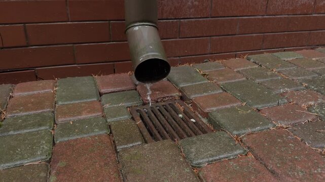 flowing water from a gutter on a brick wall and stone pavement in a neutral setting, close-up view of home maintenance work in real estate context with red and brown tones.