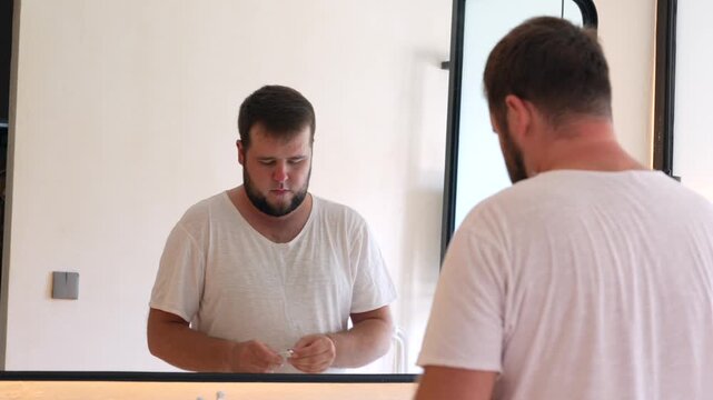 Young man applying face cream while looking in the bathroom mirror. Daily skincare routine, facial moisturizing, personal care, healthy skin and self-care at home.