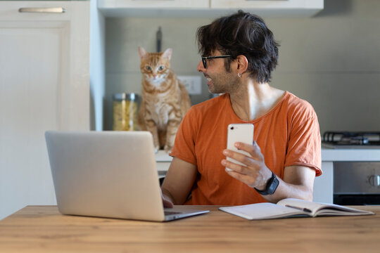 Young man using laptop at table with cute cat in home office