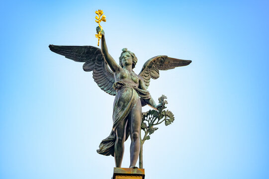 Winged bronze angel by Antonin Popp crowns a column of Cechuv Most Bridge in Prague, Czech Republic, holding a gilded branch against a clear blue sky.