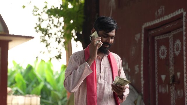 Young indian farmer talking on mobile phone while counting money 