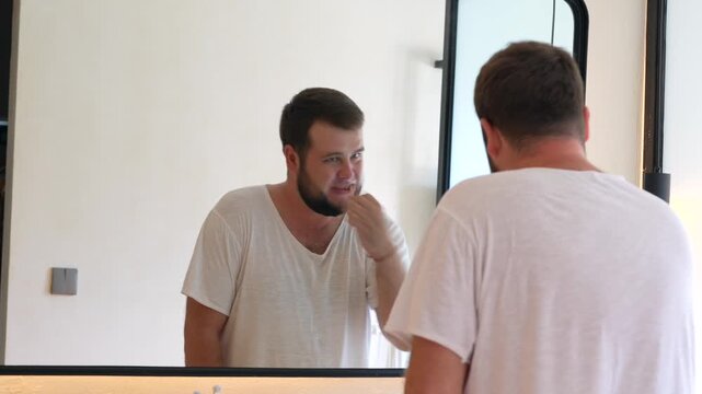 Young man brushing his teeth while looking in the bathroom mirror. Daily oral hygiene routine, personal care, healthy habits and morning self-care at home.