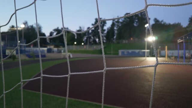 cinematic video footage presents a close-up, atmospheric view of a white soccer goal net at twilight. The sharp focus on the textured white ropes of the net contrasts beautifully 