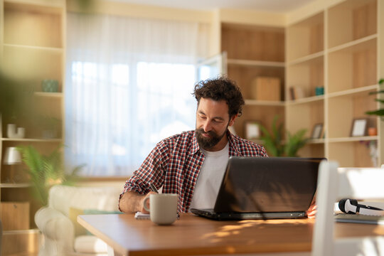 Man writing notes working from home with laptop