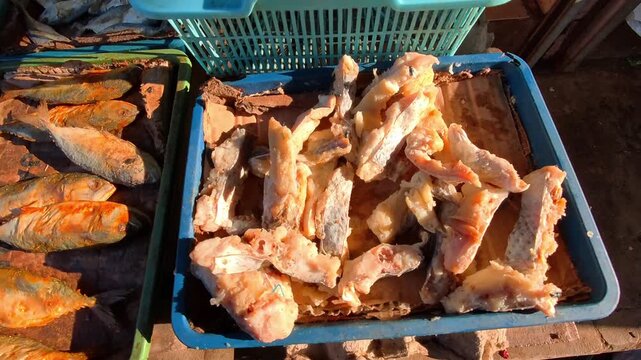 Video of Sunlit fish laid out on trays, drying in open air and surrounded by flies. Fried and dried fish in blue plastic trays. Bright light casts golden hues over drying fish. Fish Market in 4K Foota