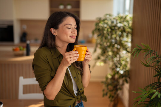 Woman enjoying morning coffee smelling aroma in kitchen