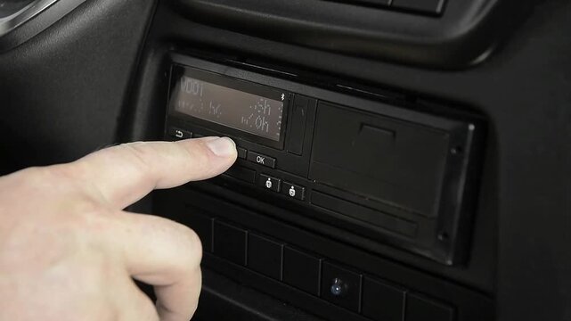 Driver hand operating digital tachograph screen in truck cabin