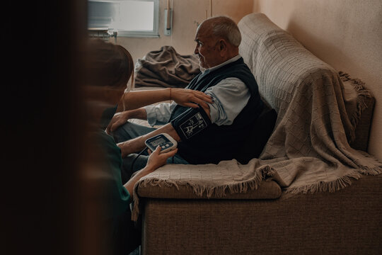 nurse checks an old man's blood pressure on a sofa at home. A warm and caring moment between patient and caregiver