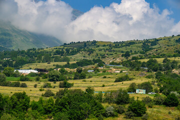 Fototapeta premium Mountain valley landscape with clouds, green slopes, and small farmhouses