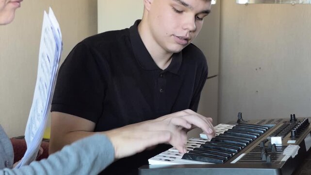 Music Teacher Guiding Teenager Boy Playing Synthesizer Keyboard in Music Lesson