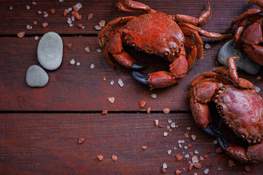 Top view of cooked red crabs with sea salt crystals and stones on dark wooden table with copy space, healthy seafood ingredient and gourmet cooking concept
