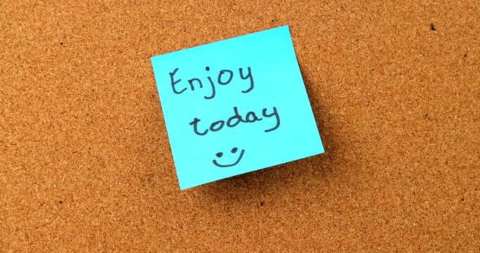 Blue Enjoy today sticky note with smiley face on cork board