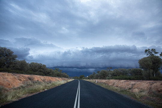 Looking down double white lines on a bitumen road towards a shelf cloud.