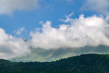 Obraz premium Clouds drift over forested mountain ridges under bright blue sky
