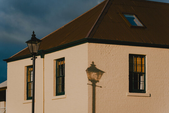 Natural light casting shadow of a streetlamp onto the pale brick wall of a heritage‑style building