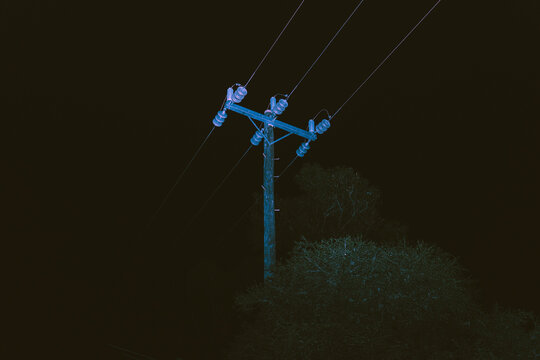 Wooden utility pole illuminated by a cool bluish light against a deep black sky