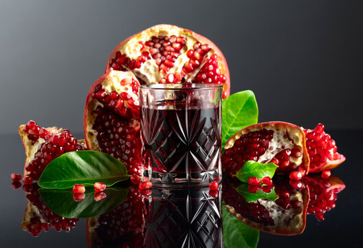 Pomegranate and a glass of ruby-red juice on a black reflective background.