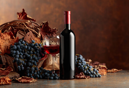 Bottle of red wine with blue grapes on a brown background.