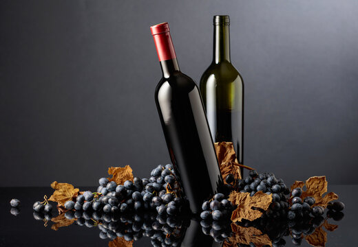 Bottles of red wine with blue grapes on a black reflective background.