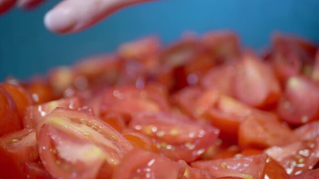 A female hand mixes fresh chopped tomatoes in a bowl, highlighting the juicy red texture in slow motion. Concept of healthy cooking preparation and fresh vegetarian ingredients.