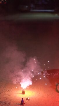 Close-up of a person using a sparkler to light an anar fountain firework during Diwali celebrations at night, with glowing flames and smoke.