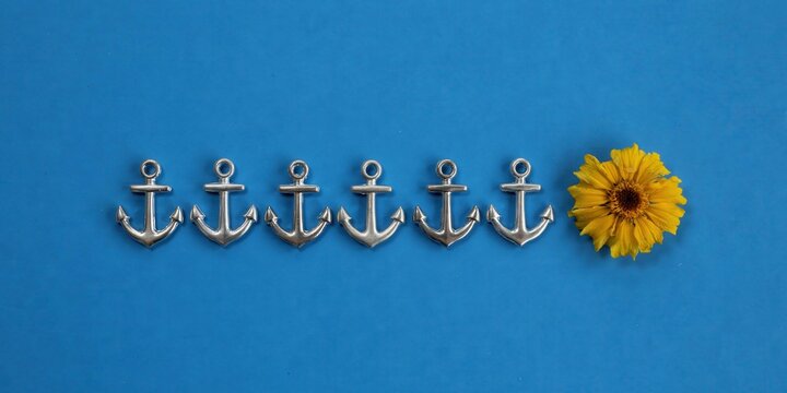 Line of silver anchors and a single yellow flower on blue background symbolizing uniqueness and standing out from a group
