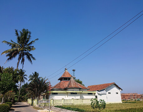 Kebumen, Central Java, Indonesia - July 18, 2026: Traditional Indonesian mosque with a distinctive red tiled roof in a rural tropical village landscape.