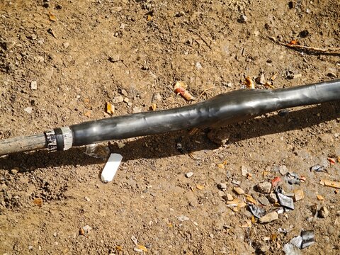 ​Close-up of an underground electrical power cable repaired with a black heat-shrink sleeve lying in a dirt trench