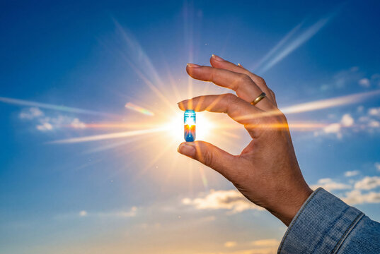 Hand holding glowing blue medical capsule against sun rays