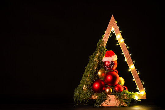 Modern DIY wooden Christmas tree with LED lights, moss, red balls and ornaments on a neutral background