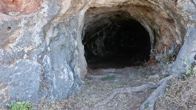 Close up view of World War II cave shelter carved into rocky cliff on Crete with dark tunnel entrance. Crete. Greece.