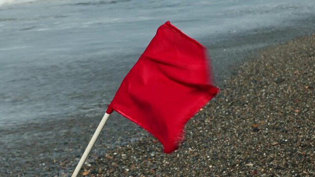 Close-up view of red warning flag on pebble beach with storm waves on Cretan Sea coast. Crete. Greece. 