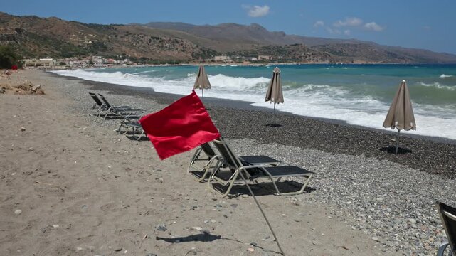 View of red warning flag on pebble beach with storm waves on Cretan Sea coast. Crete. Greece. 