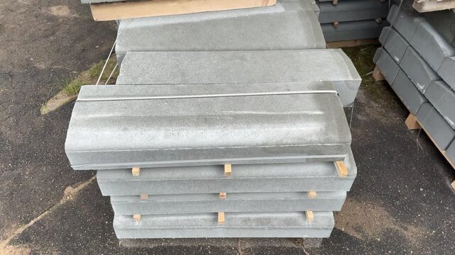 Stacked grey concrete coping stones on wooden pallets outdoors, building materials for construction and landscaping, heavy masonry blocks