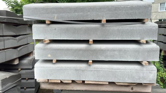 Stacked grey concrete slabs on wooden pallets outdoors, heavy building materials for construction and landscaping, masonry blocks ready for transport, construction material, landscaping supply