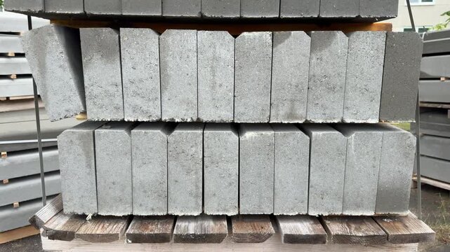 Stacked grey concrete curbstones on wooden pallet outdoors, building materials for road construction, masonry blocks, construction material, paving block