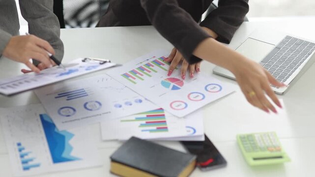 Two business professionals collaborating in a modern office, analyzing financial performance data, charts, and graphs on paper reports and a digital tablet to discuss business strategy.