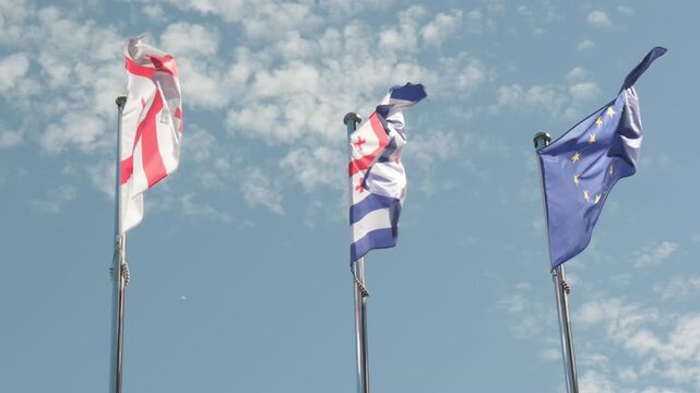 Flags of Europe, Georgia and Autonomous Republic of Adjara flutter against background clear blue sky with clouds