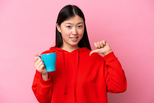 Young Chinese woman holding cup of coffee isolated on pink background proud and self-satisfied