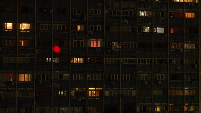 Night facade of a large apartment building with multiple floors where the lights in the windows randomly turn on and off, suggesting the daily life of the residents inside the apartments time lapse