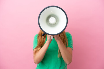 Young blonde woman isolated on pink background shouting through a megaphone to announce something