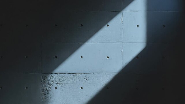 Sunlight casting a diagonal shadow on a raw concrete wall, creating an abstract architectural background with light moving across the textured surface of the cement blocks