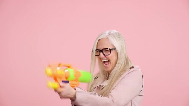 Playful senior woman shooting a water gun