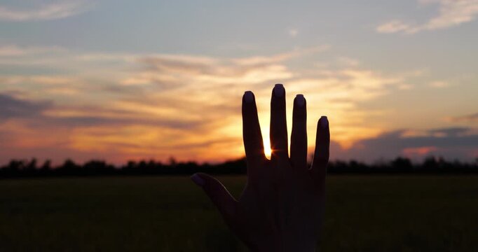 Female hand reaches toward glowing sunset over rural landscape. Vertical video represents dreams, inspiration, personal aspirations and the pursuit of goals in a serene natural setting.