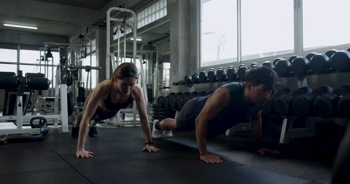 Young Asian couple trains push ups side by side in modern gym, lowering and rising together before kneeling for recovery, sharing support, motivation, wellness, healthy fitness teamwork routine