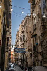 Fototapeta premium Naples, italy. December 29, 2024. Buildings lining a narrow street in the historic center of naples, italy, with laundry drying on balconies and string lights overhead