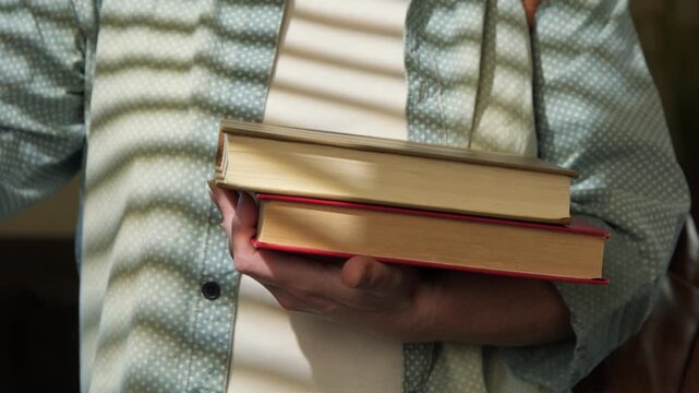 Woman student puts textbooks in stack of books in her hands close-up